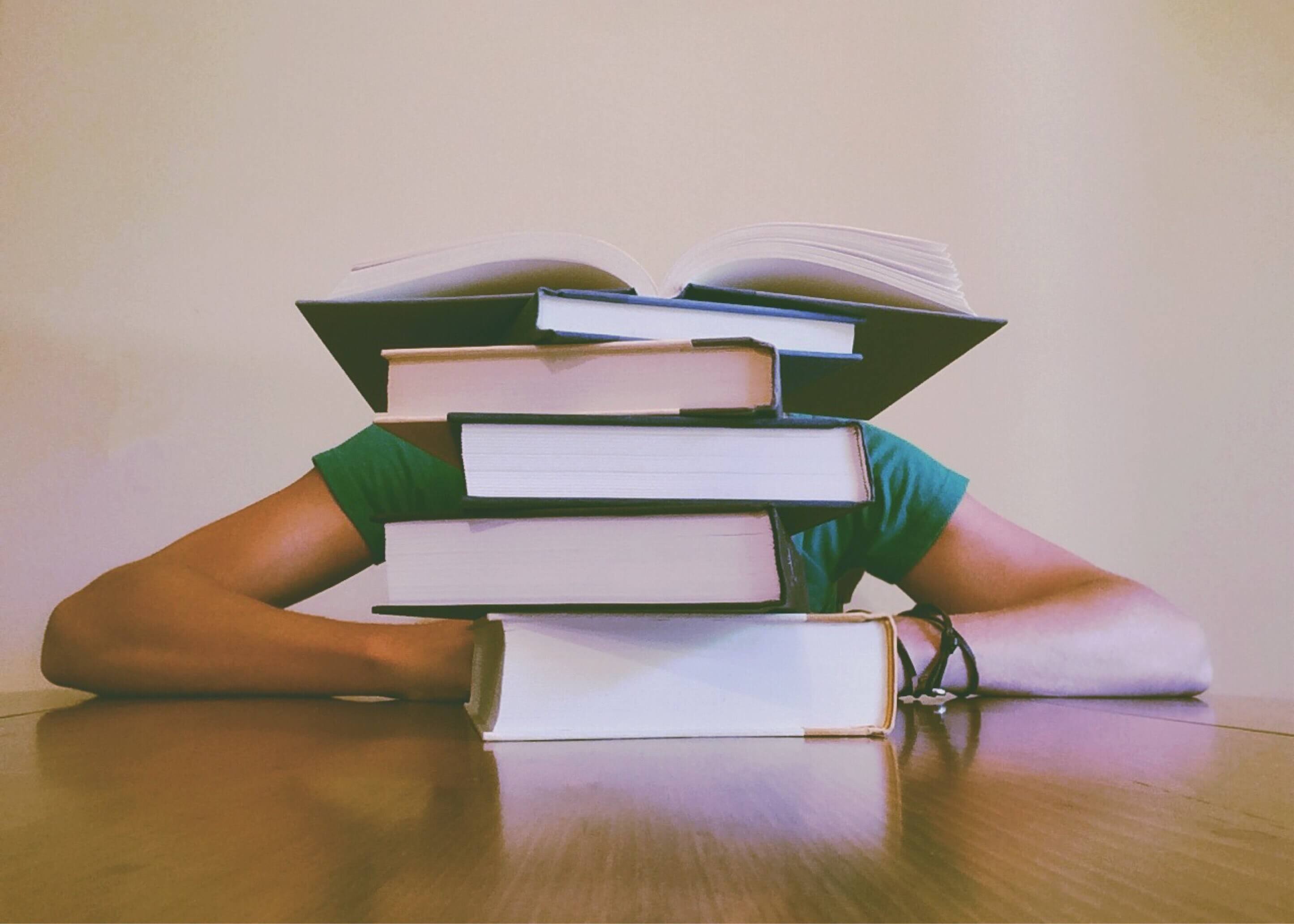 Pile of books on a desk with a person studying behind it.