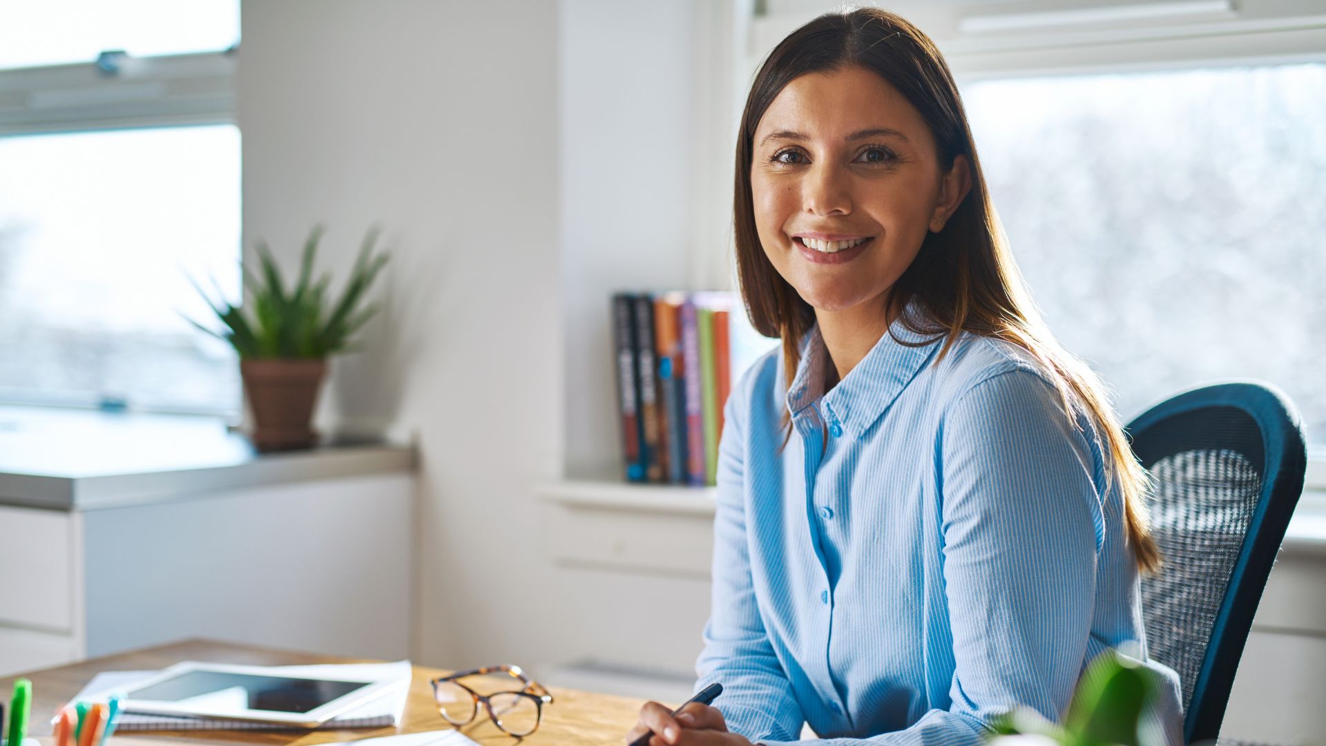 Professional woman in blue shirt sitting at desk, smiling at camera