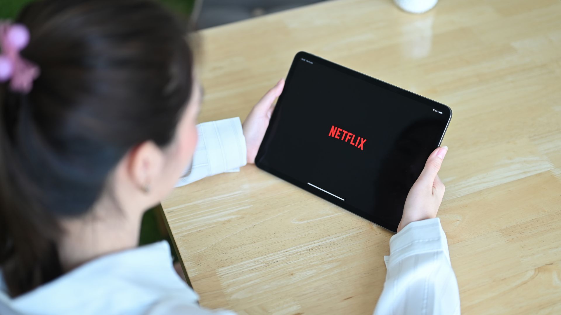 A professional woman sitting at a table, opening Netflix on a tablet, getting ready to catch up on her favourite lawyer series wherever possible in her busy schedule