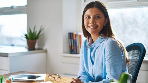 Professional woman in blue shirt sitting at desk, smiling at camera